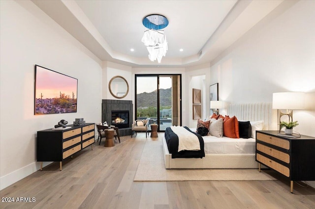 bedroom with a mountain view, wood-type flooring, a tray ceiling, and access to outside