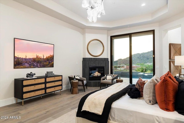 bedroom with a raised ceiling, a mountain view, a tiled fireplace, hardwood / wood-style floors, and access to exterior