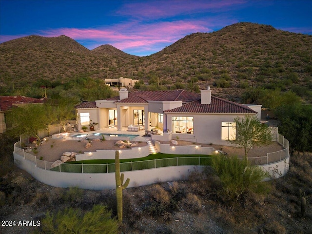 back house at dusk with a mountain view and a fenced in pool