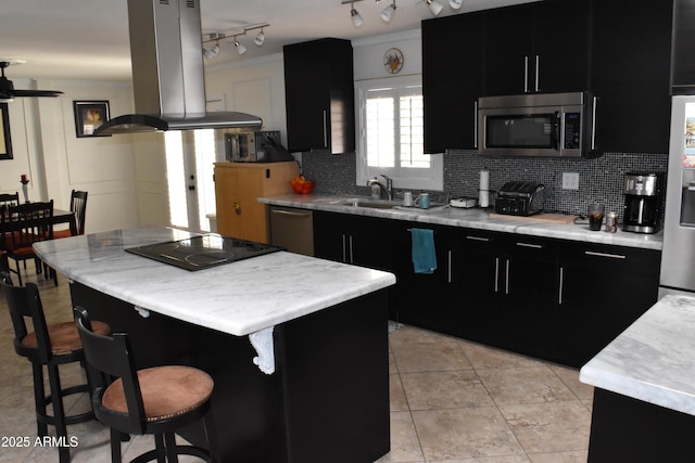 kitchen featuring island exhaust hood, a sink, dark cabinetry, appliances with stainless steel finishes, and a kitchen bar