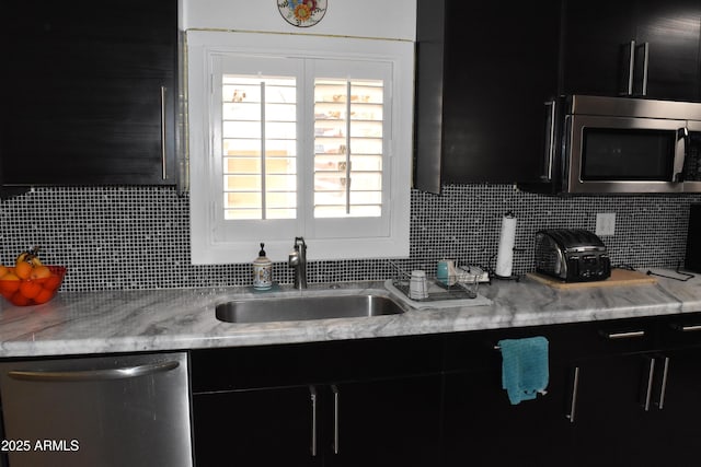 kitchen with dark cabinets, tasteful backsplash, appliances with stainless steel finishes, and a sink