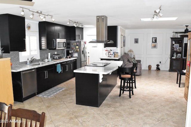 kitchen featuring a decorative wall, stainless steel appliances, dark cabinetry, backsplash, and island exhaust hood