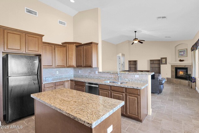 kitchen featuring sink, a tile fireplace, a center island, dishwasher, and black fridge