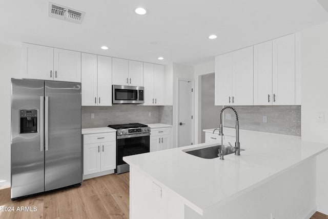 kitchen featuring white cabinetry, sink, light hardwood / wood-style flooring, kitchen peninsula, and appliances with stainless steel finishes