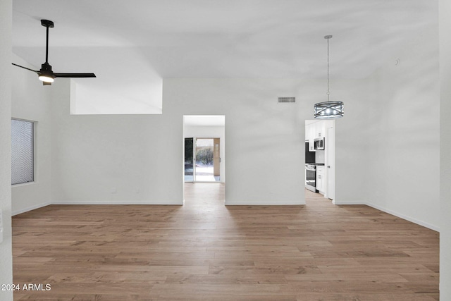 unfurnished living room featuring ceiling fan, light hardwood / wood-style floors, and a high ceiling