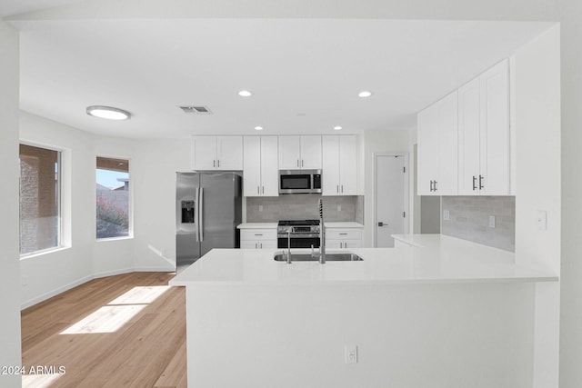 kitchen with white cabinetry, kitchen peninsula, appliances with stainless steel finishes, and light hardwood / wood-style flooring