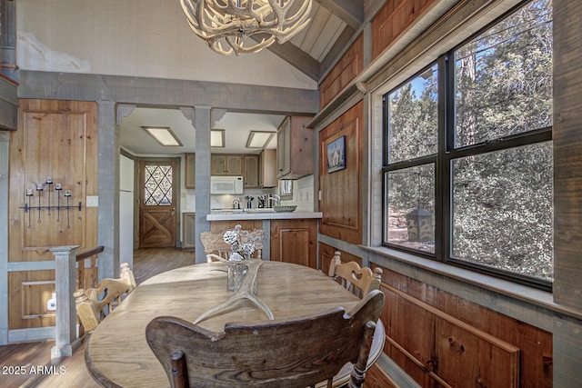 dining space featuring light wood-style floors, a chandelier, vaulted ceiling, and ornate columns