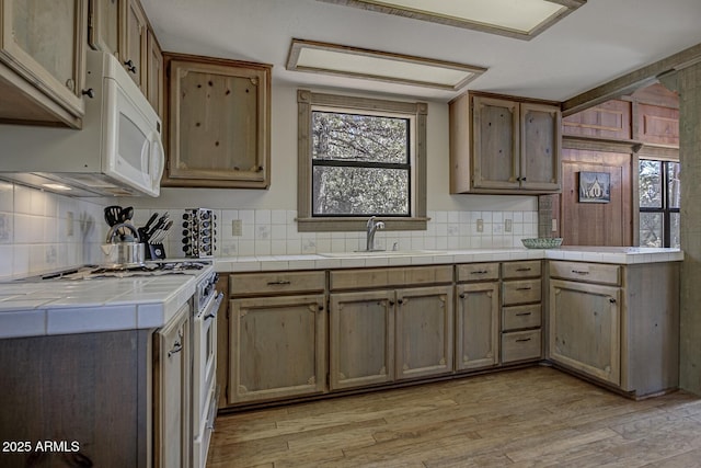 kitchen with range with gas stovetop, tile countertops, light wood-style flooring, a sink, and backsplash