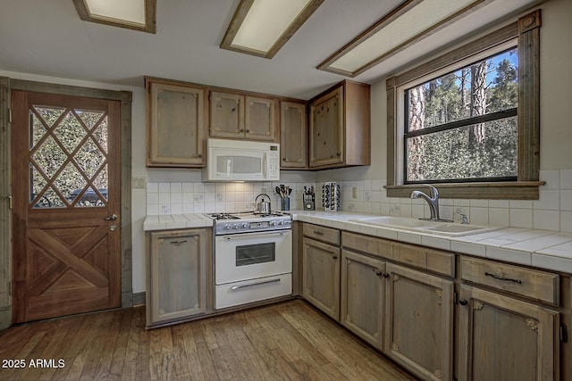 kitchen with tile countertops, white appliances, a sink, backsplash, and wood-type flooring