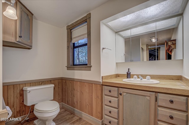 bathroom featuring toilet, a wainscoted wall, wood finished floors, vanity, and wood walls