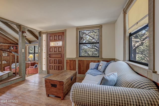 living area with a wainscoted wall, lofted ceiling with beams, light wood-type flooring, and wooden walls