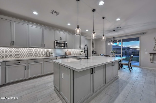 kitchen with stainless steel microwave, backsplash, visible vents, and gray cabinetry