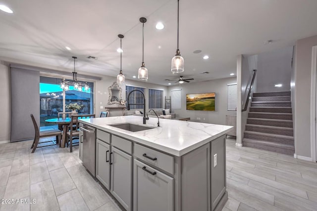 kitchen featuring a center island with sink, hanging light fixtures, gray cabinetry, open floor plan, and a sink