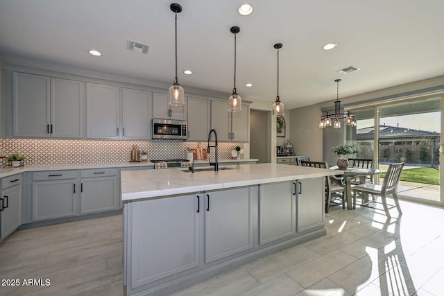 kitchen with a sink, tasteful backsplash, stainless steel microwave, and gray cabinets