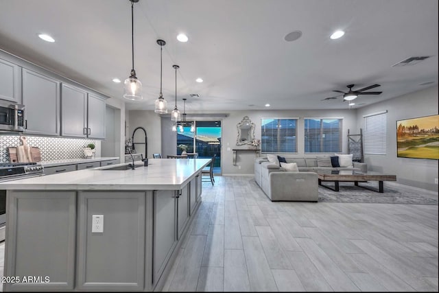 kitchen featuring a center island with sink, stainless steel appliances, tasteful backsplash, gray cabinetry, and a sink