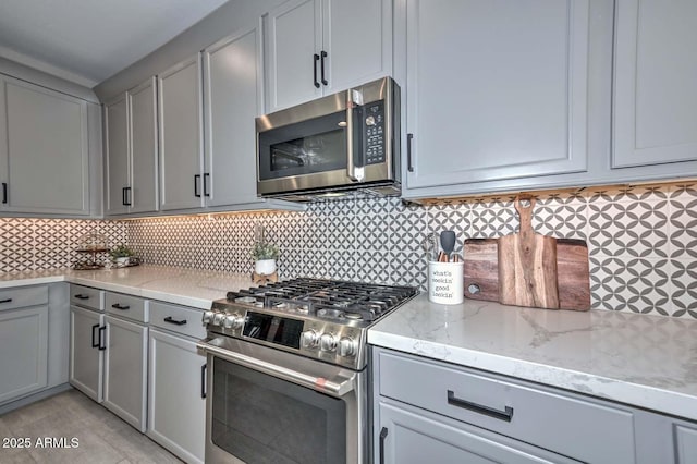 kitchen featuring stainless steel appliances, light stone counters, backsplash, and gray cabinets