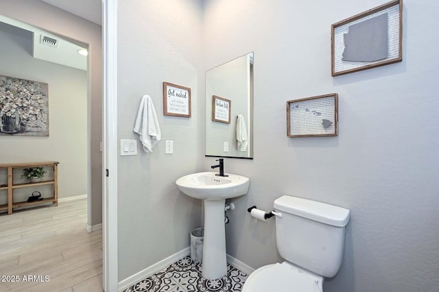 half bathroom with baseboards, visible vents, toilet, wood finished floors, and a sink