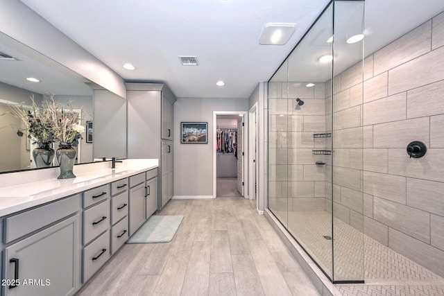 full bath featuring a sink, wood finished floors, visible vents, double vanity, and a stall shower