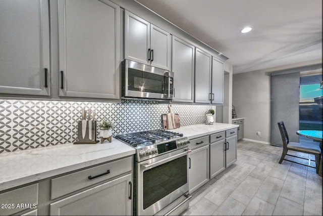 kitchen with light stone counters, stainless steel appliances, gray cabinets, decorative backsplash, and baseboards