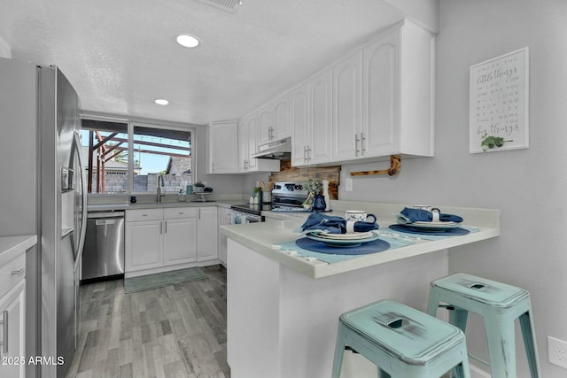 kitchen featuring a peninsula, white cabinetry, appliances with stainless steel finishes, and under cabinet range hood