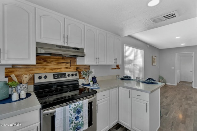kitchen featuring visible vents, a peninsula, under cabinet range hood, white cabinets, and stainless steel electric stove