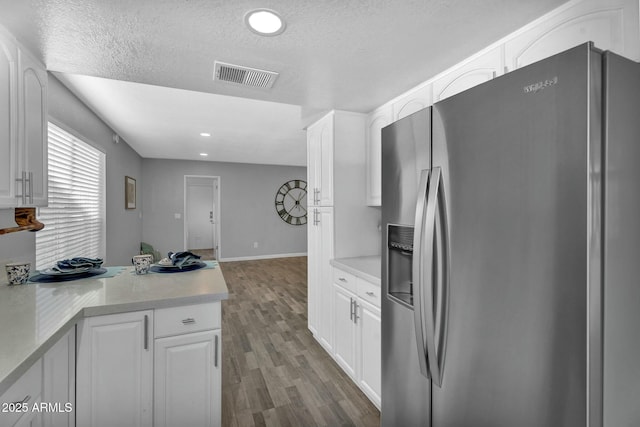 kitchen with stainless steel refrigerator with ice dispenser, visible vents, white cabinetry, and wood finished floors