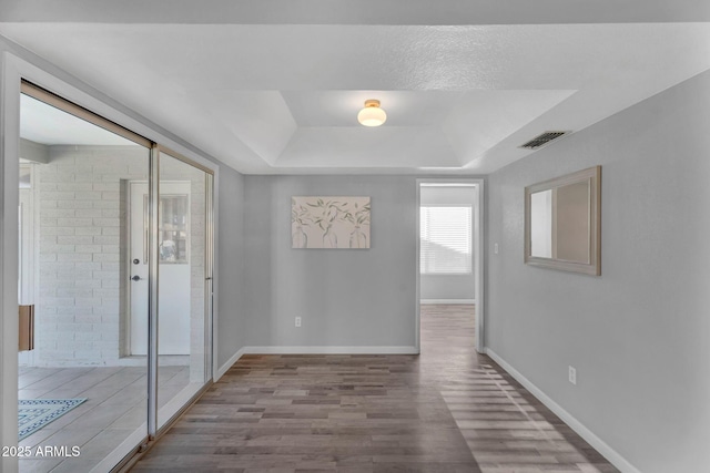 empty room featuring visible vents, baseboards, a raised ceiling, and wood finished floors