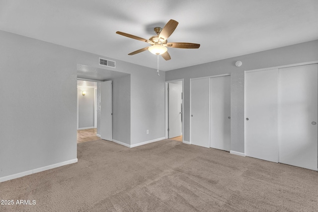 unfurnished bedroom with baseboards, two closets, carpet flooring, and visible vents
