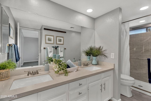 bathroom with double vanity, a sink, a stall shower, and toilet