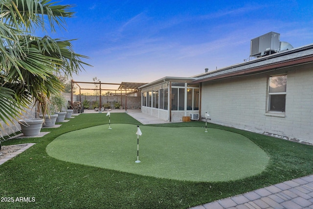 yard at dusk with a fenced backyard, a patio, a sunroom, and central AC