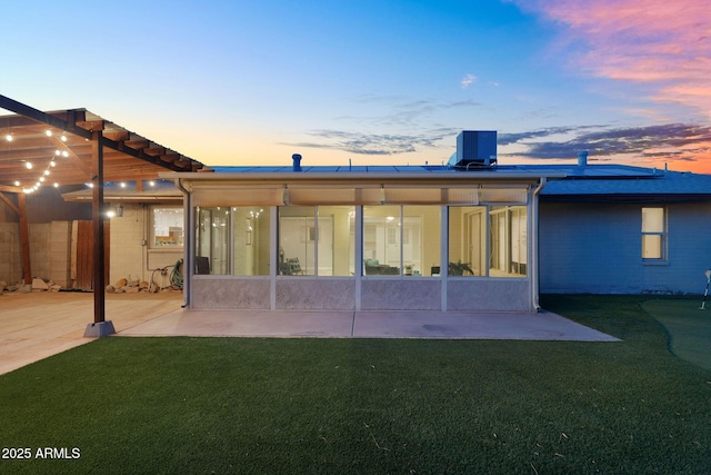 rear view of house with a sunroom, central AC, roof mounted solar panels, a yard, and a patio