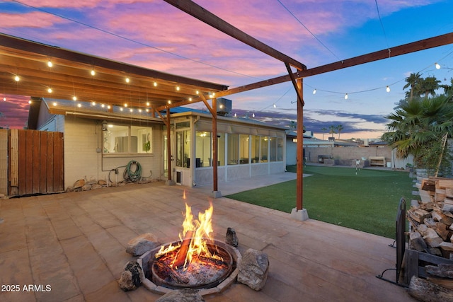 patio terrace at dusk featuring a fenced backyard, a sunroom, and an outdoor fire pit