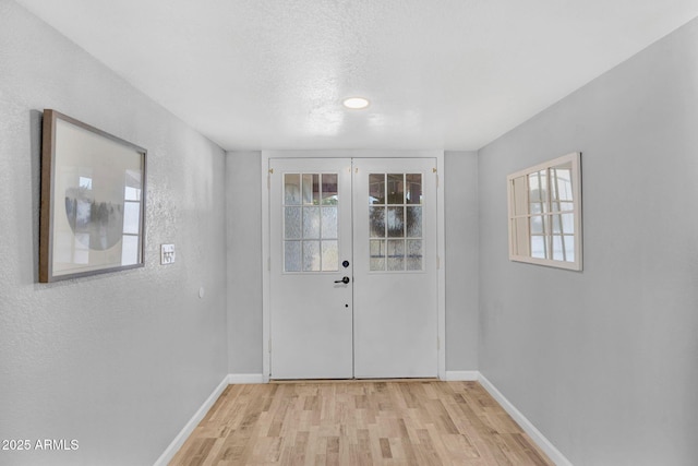 doorway with french doors, a textured ceiling, baseboards, and light wood-style flooring