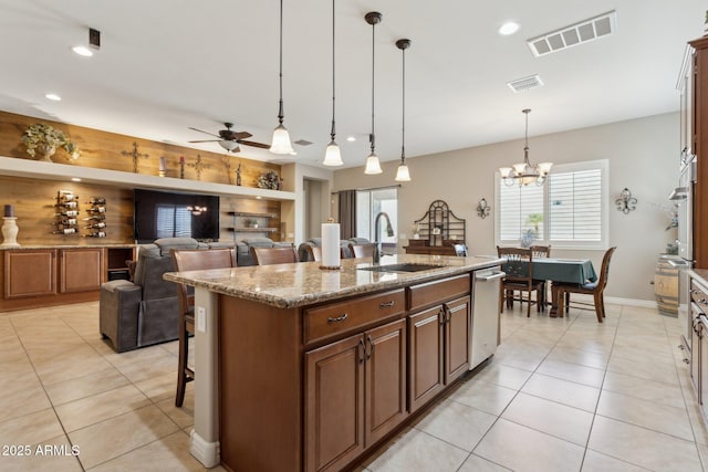 kitchen featuring light stone countertops, decorative light fixtures, an island with sink, ceiling fan with notable chandelier, and sink