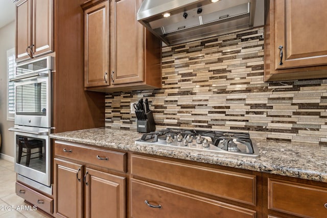 kitchen with appliances with stainless steel finishes, extractor fan, backsplash, and light stone countertops