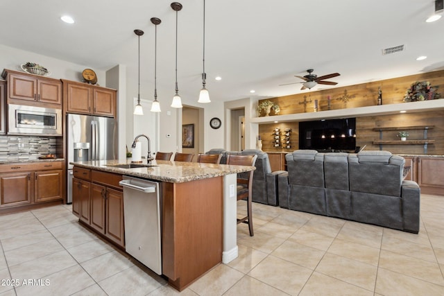 kitchen featuring a kitchen island with sink, stainless steel appliances, ceiling fan, a kitchen bar, and sink