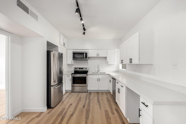 kitchen with sink, white cabinets, light hardwood / wood-style floors, stainless steel appliances, and a textured ceiling