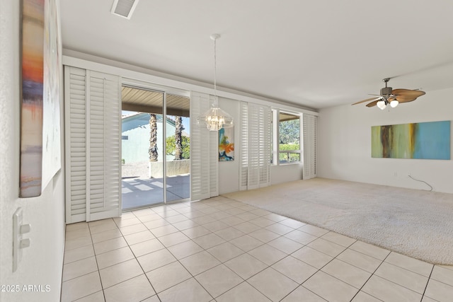 spare room with light carpet, light tile patterned floors, ceiling fan with notable chandelier, and visible vents