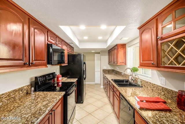 kitchen featuring a sink, black appliances, glass insert cabinets, stone counters, and a tray ceiling