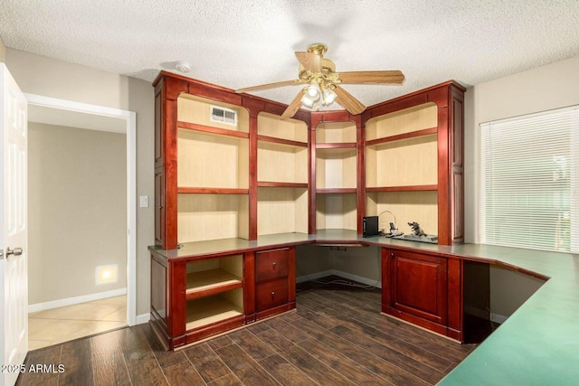 unfurnished office featuring built in desk, a textured ceiling, visible vents, dark wood-type flooring, and ceiling fan