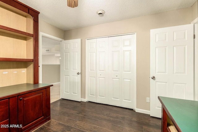 unfurnished office with baseboards, visible vents, a textured ceiling, and dark wood-type flooring