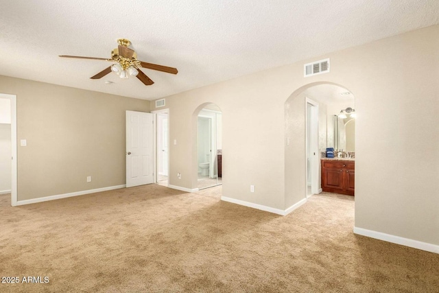 interior space with arched walkways, light colored carpet, visible vents, and a ceiling fan