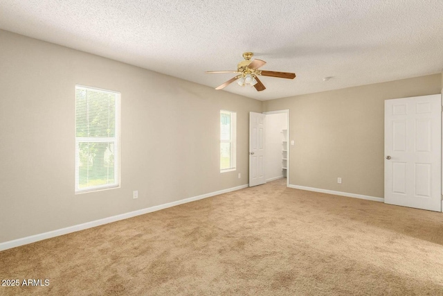 empty room with baseboards, a textured ceiling, ceiling fan, and light colored carpet