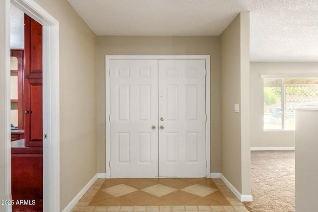 foyer entrance with baseboards, a textured ceiling, light tile patterned floors, and light colored carpet