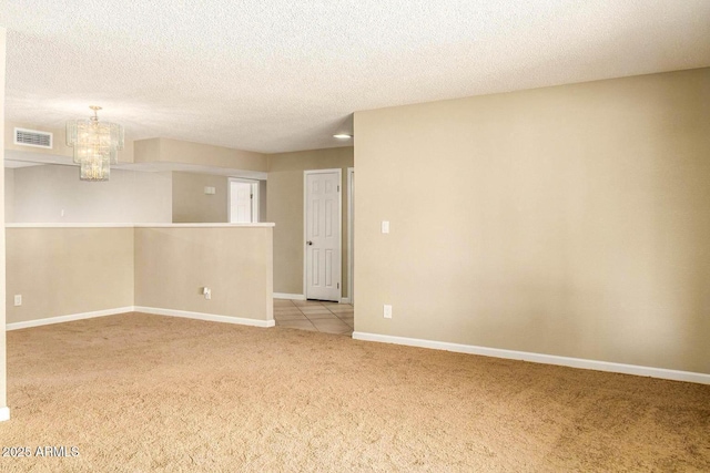 empty room with an inviting chandelier, a textured ceiling, visible vents, baseboards, and light carpet