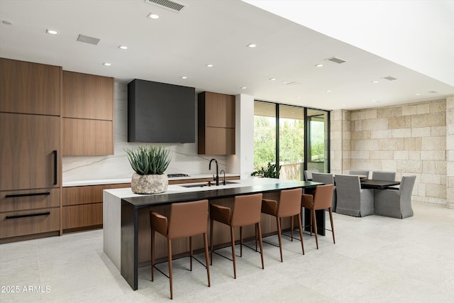 kitchen with a kitchen bar, sink, a kitchen island with sink, and backsplash