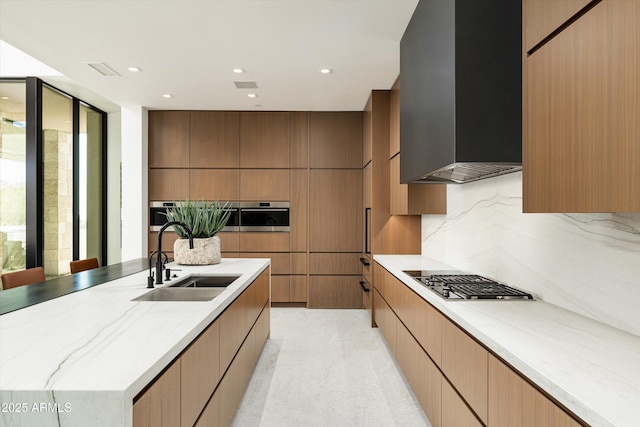 kitchen featuring sink, backsplash, wall chimney exhaust hood, light stone countertops, and stainless steel oven