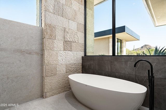 bathroom featuring tile patterned flooring, a bath, and tile walls