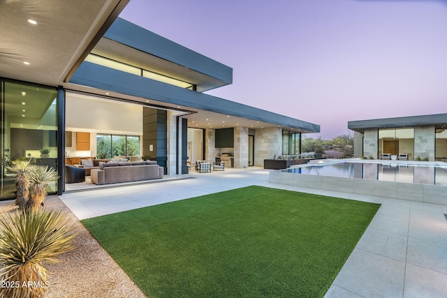 back house at dusk featuring a yard, a patio area, and outdoor lounge area