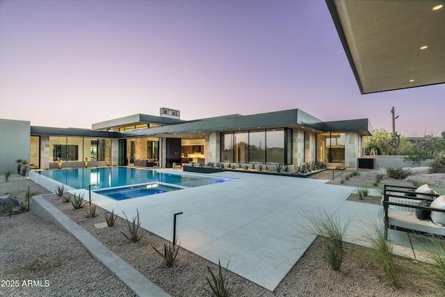 pool at dusk featuring an in ground hot tub and a patio